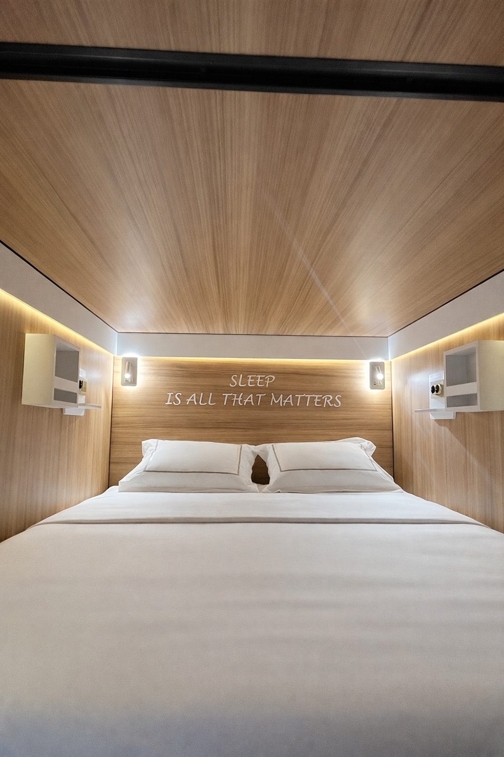 SleepPod Oak sleeping space with double bed, wood ceiling and wall-mounted reading lights