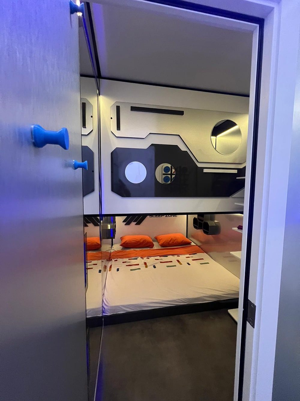 SleepPod Space lower sleeping area seen through the open door, with orange cushions